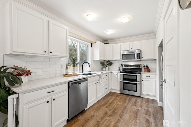 kitchen with light countertops, appliances with stainless steel finishes, white cabinetry, a sink, and light wood-type flooring