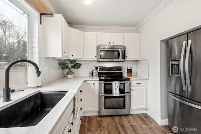 kitchen featuring tasteful backsplash, white cabinets, wood finished floors, stainless steel appliances, and a sink