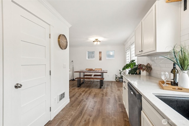 kitchen featuring wood finished floors, white cabinets, decorative backsplash, dishwasher, and crown molding