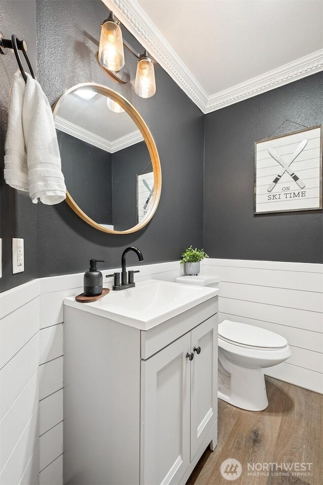 bathroom featuring toilet, a wainscoted wall, ornamental molding, wood finished floors, and vanity