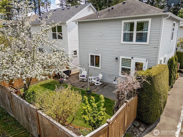 rear view of house featuring a fenced backyard, roof with shingles, a patio area, and a yard