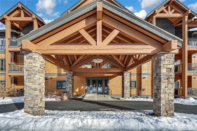 snow covered property entrance featuring french doors and brick siding