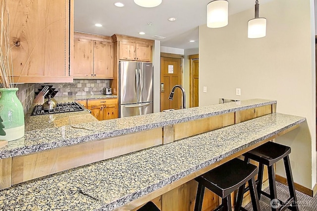 kitchen with a peninsula, a sink, stainless steel refrigerator, and backsplash