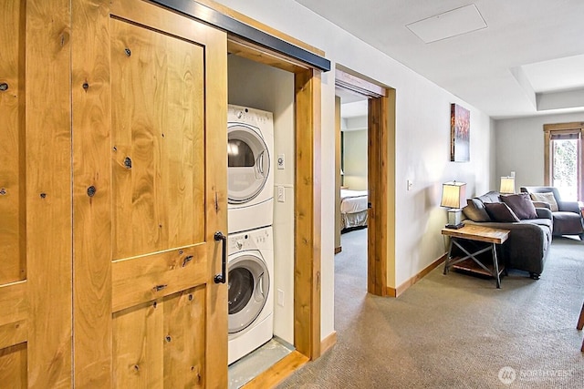 washroom with stacked washer and dryer, laundry area, light colored carpet, and baseboards