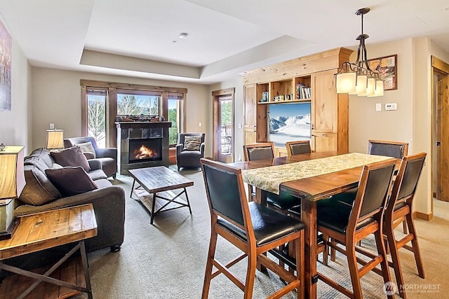 dining space featuring a warm lit fireplace, a raised ceiling, and light carpet