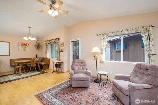 living area featuring baseboards, ceiling fan with notable chandelier, wood finished floors, and vaulted ceiling