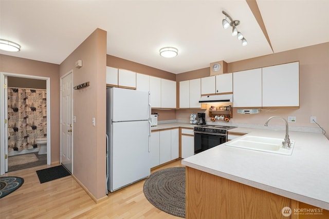 kitchen featuring black electric range oven, a sink, under cabinet range hood, freestanding refrigerator, and light countertops