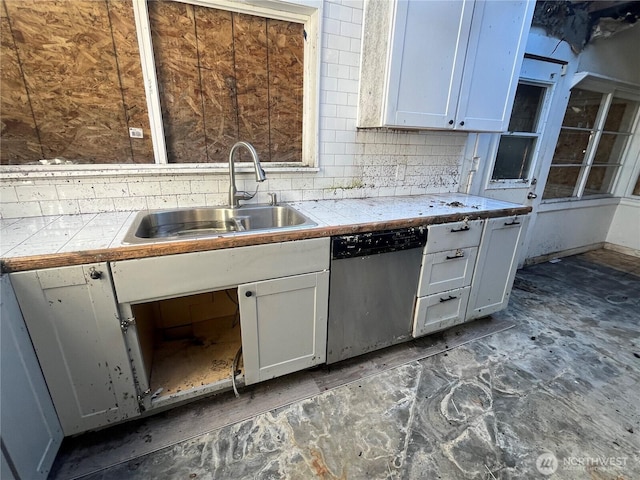 kitchen with tile countertops, tasteful backsplash, stainless steel dishwasher, white cabinetry, and a sink