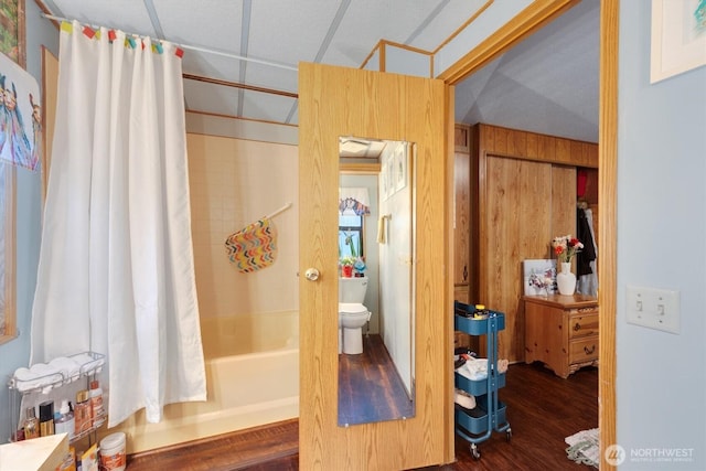 bathroom featuring toilet, wooden walls, shower / bath combination with curtain, and wood finished floors