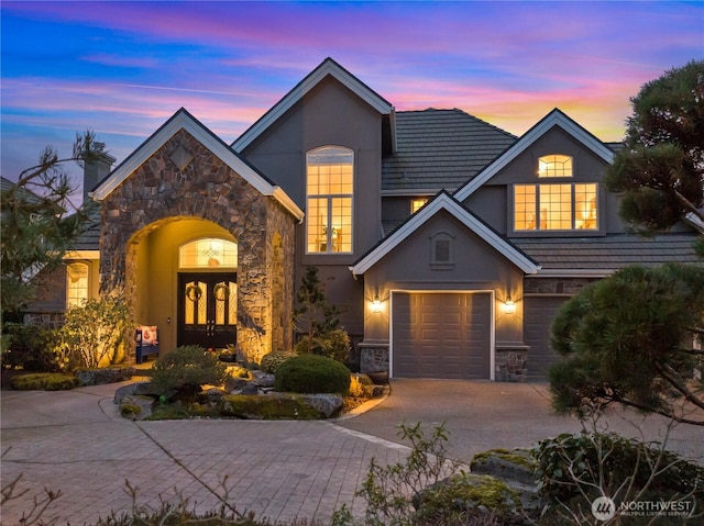 view of front of home featuring driveway, french doors, stone siding, and stucco siding