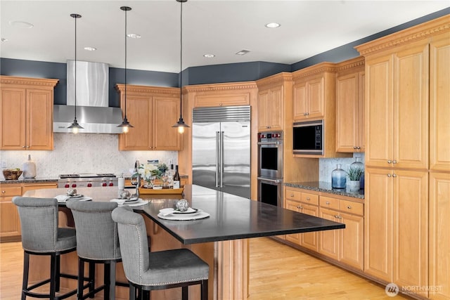 kitchen featuring light wood finished floors, wall chimney exhaust hood, a center island with sink, and built in appliances