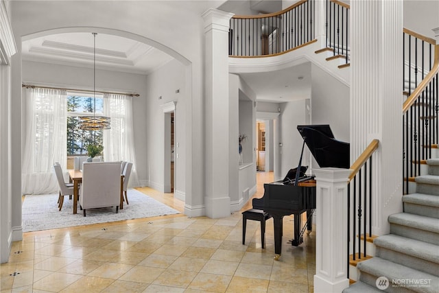 foyer entrance with crown molding, light tile patterned floors, a raised ceiling, a towering ceiling, and stairs