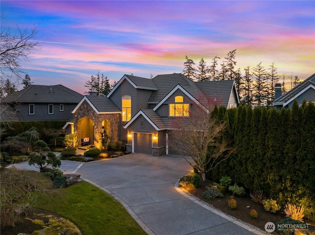 view of front of home with stucco siding, an attached garage, stone siding, driveway, and a tiled roof