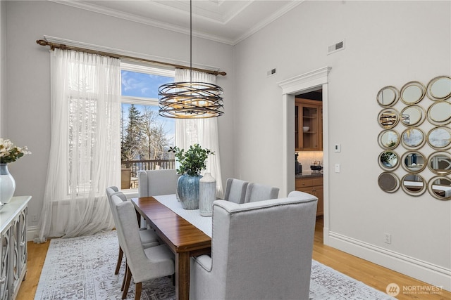 dining room featuring a notable chandelier, visible vents, light wood-style floors, ornamental molding, and baseboards