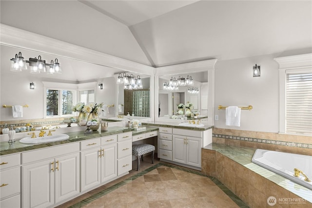 bathroom featuring tiled bath, vaulted ceiling, and vanity