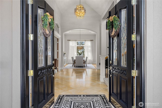 entryway with arched walkways, light tile patterned floors, an inviting chandelier, high vaulted ceiling, and baseboards