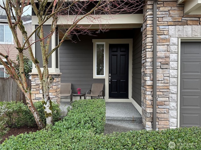 view of exterior entry with stone siding, a porch, a garage, and fence