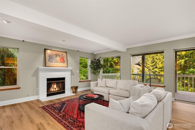 living area featuring light wood-style floors, a brick fireplace, baseboards, and beamed ceiling