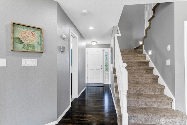 entrance foyer featuring a textured wall, dark wood finished floors, baseboards, and stairs