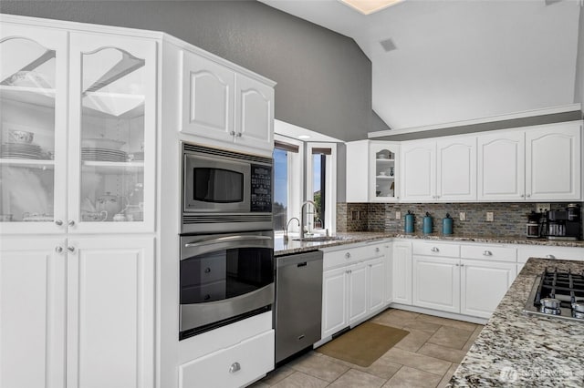 kitchen featuring lofted ceiling, light stone counters, a sink, appliances with stainless steel finishes, and glass insert cabinets