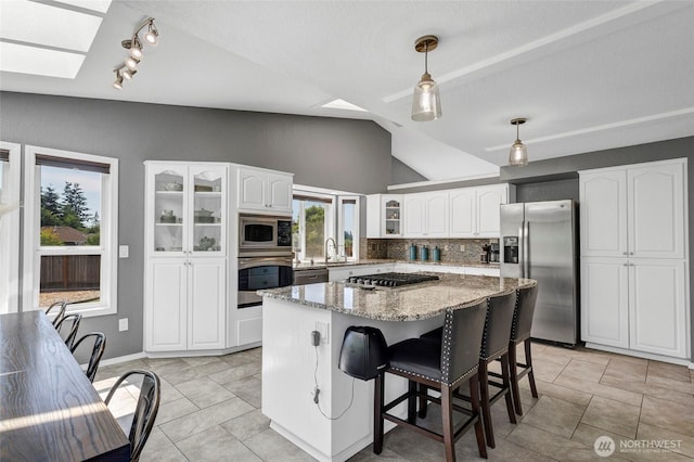 kitchen with tasteful backsplash, glass insert cabinets, a center island, stainless steel appliances, and a sink