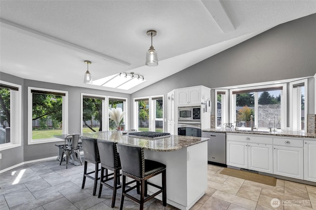 kitchen with light stone counters, lofted ceiling, appliances with stainless steel finishes, white cabinetry, and a kitchen island