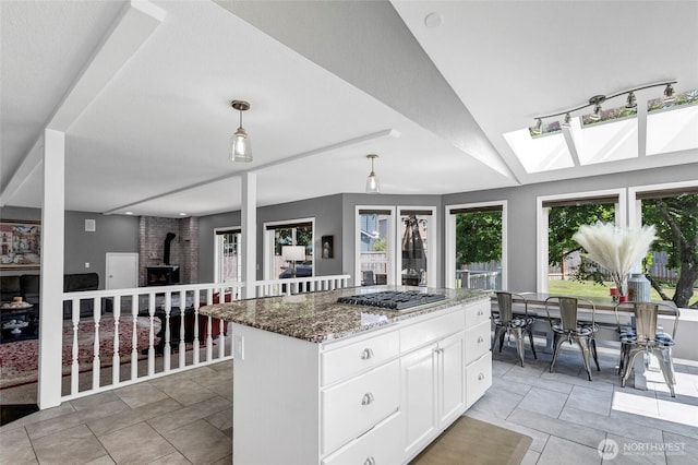 kitchen with dark stone countertops, decorative light fixtures, a wood stove, stainless steel gas stovetop, and white cabinetry