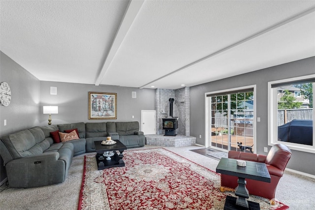 living room with baseboards, beamed ceiling, a wood stove, a textured ceiling, and carpet floors