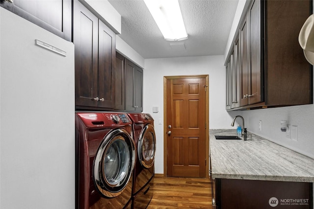 laundry area with cabinet space, wood finished floors, a textured ceiling, washing machine and dryer, and a sink