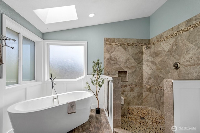 bathroom with a freestanding bath, vaulted ceiling with skylight, tiled shower, and wood finished floors