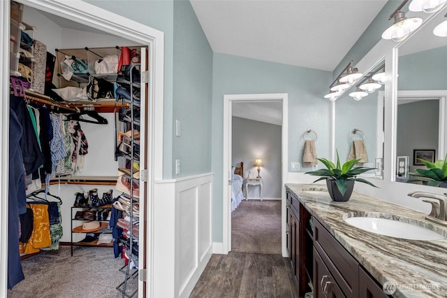 full bath with lofted ceiling, wood finished floors, a sink, double vanity, and a walk in closet