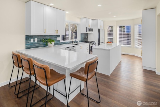 kitchen featuring decorative backsplash, appliances with stainless steel finishes, a breakfast bar, dark wood-type flooring, and a center island