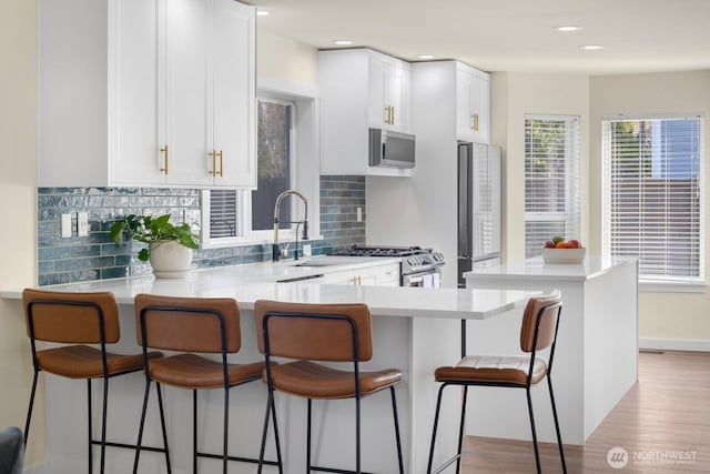 kitchen featuring tasteful backsplash, white cabinets, appliances with stainless steel finishes, a kitchen breakfast bar, and light countertops