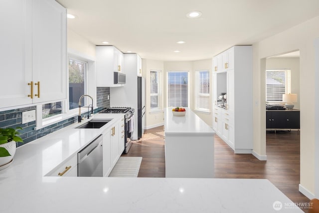 kitchen with dark wood-type flooring, a sink, light countertops, appliances with stainless steel finishes, and backsplash