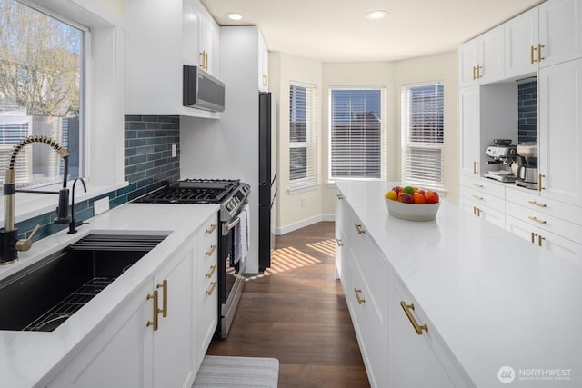 kitchen with a sink, white cabinets, appliances with stainless steel finishes, decorative backsplash, and dark wood-style floors