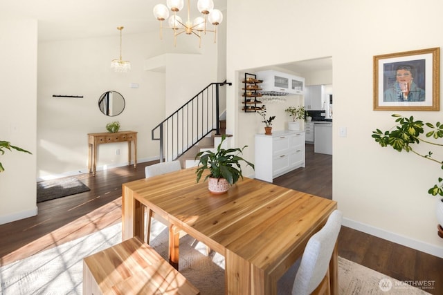 dining room with dark wood-style floors, a high ceiling, a chandelier, baseboards, and stairs