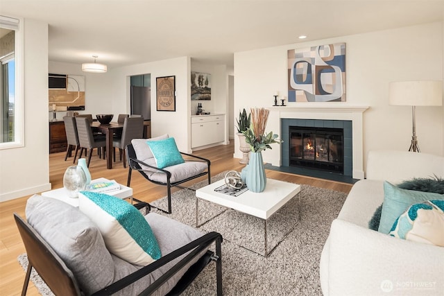 living area with a tiled fireplace, light wood-type flooring, and baseboards