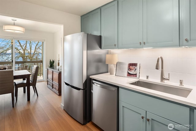 kitchen with a sink, backsplash, stainless steel appliances, light wood-style floors, and light countertops