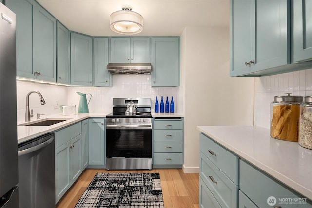 kitchen with under cabinet range hood, light countertops, light wood-style flooring, stainless steel appliances, and a sink