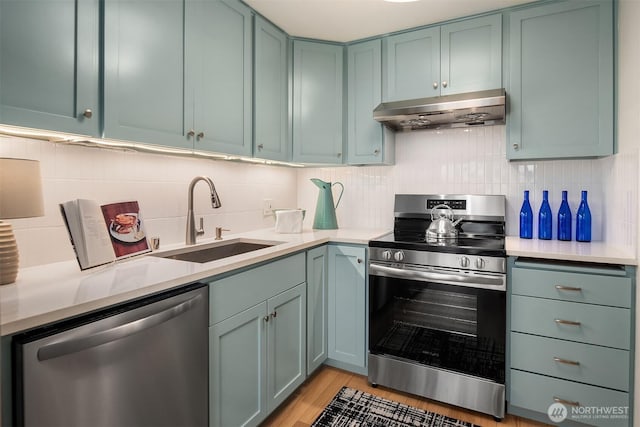 kitchen with a sink, light countertops, under cabinet range hood, and stainless steel appliances