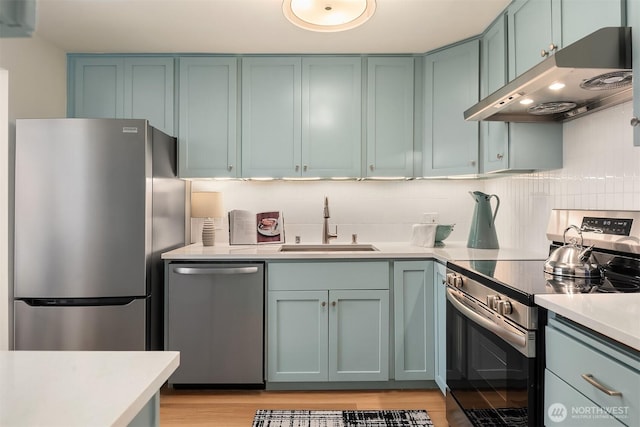 kitchen featuring under cabinet range hood, a sink, appliances with stainless steel finishes, light countertops, and decorative backsplash