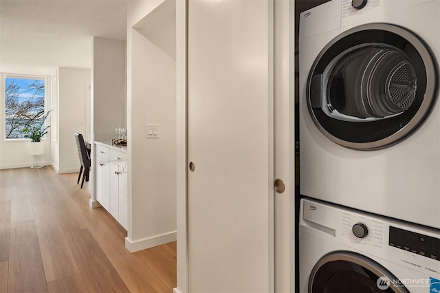 washroom featuring baseboards, light wood-style floors, and stacked washer and dryer