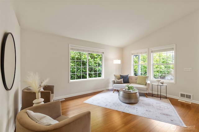 living area featuring visible vents, baseboards, lofted ceiling, and wood finished floors