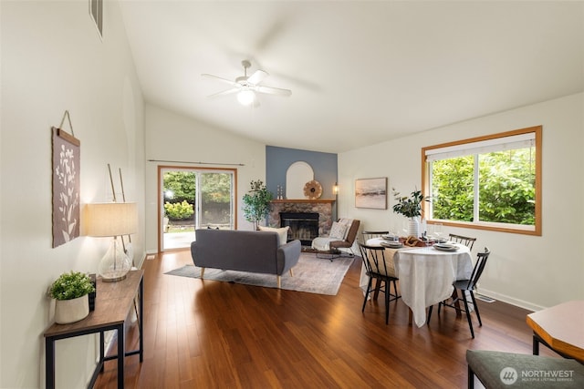 dining space with dark wood finished floors, a stone fireplace, a healthy amount of sunlight, and visible vents