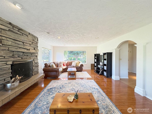 living room with arched walkways, a textured ceiling, a fireplace, and wood finished floors