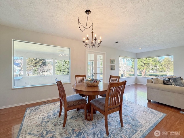 dining space featuring a chandelier, wood finished floors, visible vents, baseboards, and french doors