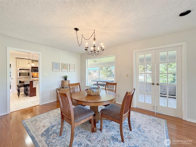 dining room with a textured ceiling, french doors, light wood finished floors, and a notable chandelier