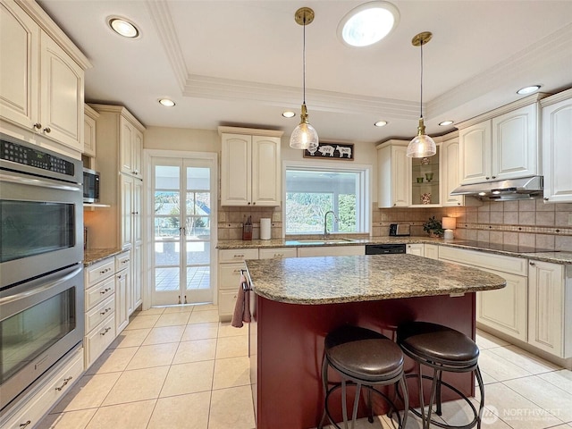 kitchen featuring light tile patterned floors, under cabinet range hood, a sink, black appliances, and a tray ceiling