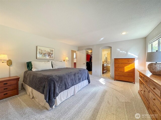 bedroom with arched walkways, a textured ceiling, light carpet, a closet, and a walk in closet