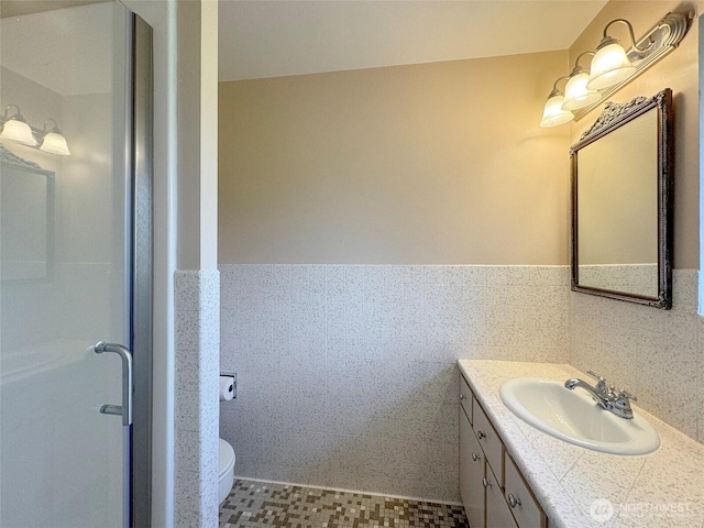 bathroom featuring toilet, vanity, tile walls, and wainscoting